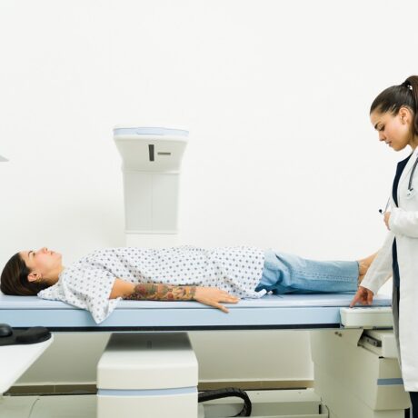 Femeie întinsă pe o masă de osteodensitometrie și medic lângă masă care o pregătește pentru investigație