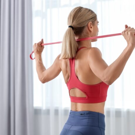 O femeie tânără care face exerciții fizice cu o bandă elastică într-o cameră
